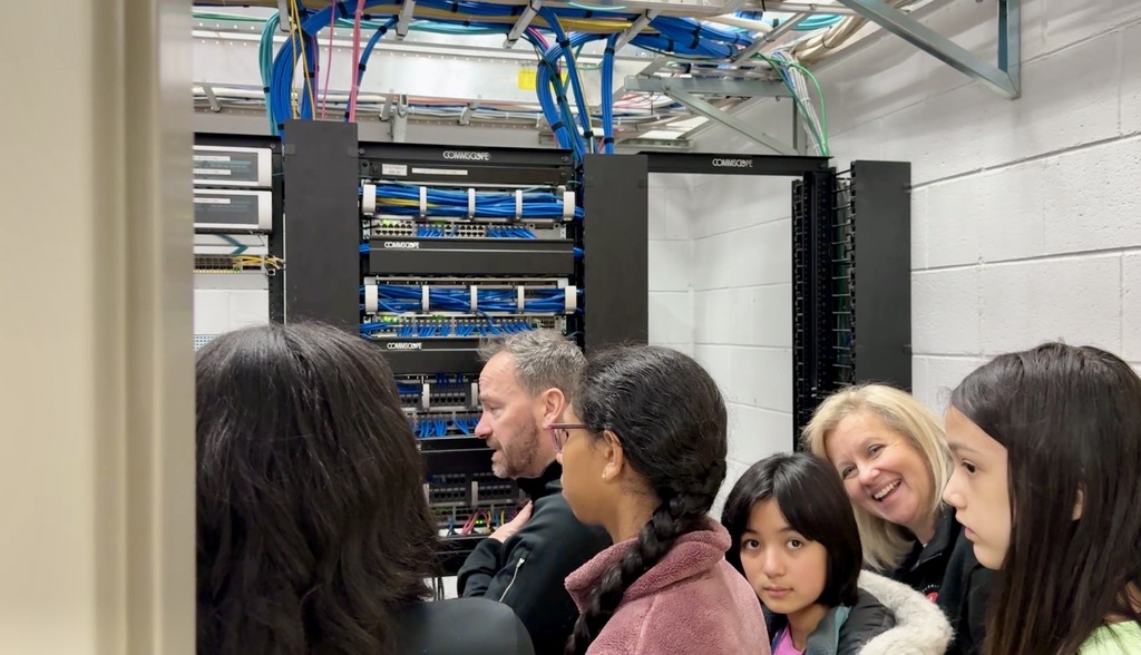 Group of people observing a server rack with organized network cables in a data center room.