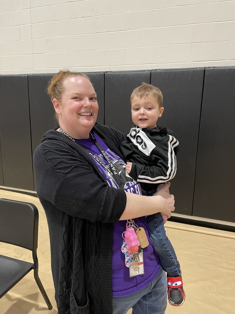 Adult holding a young child in a gymnasium with black padded walls and a chair nearby.