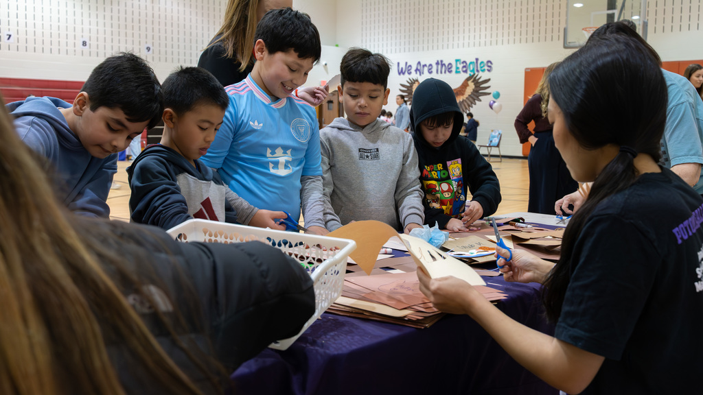 Children gathered around a table in a gymnasium, engaging in a group activity with paper bags and markers.
