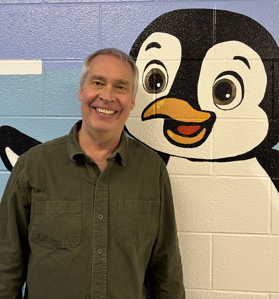 Alan Skubal in a green shirt standing in front of a cartoon penguin mural on a painted brick wall.