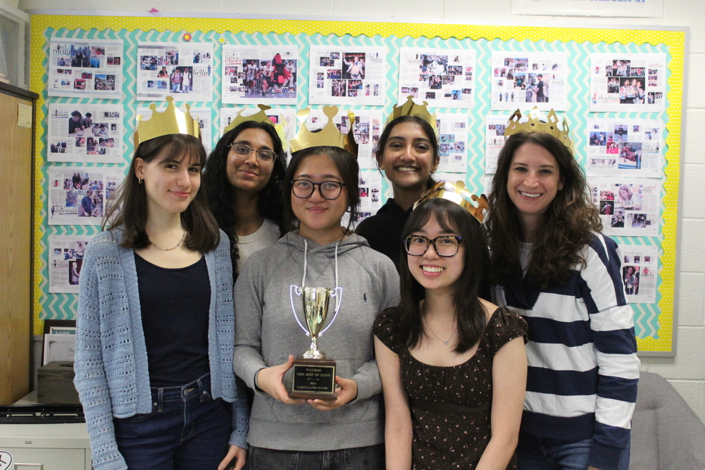 Group of six young people wearing gold paper crowns posing indoors with a trophy held by the person in the center.