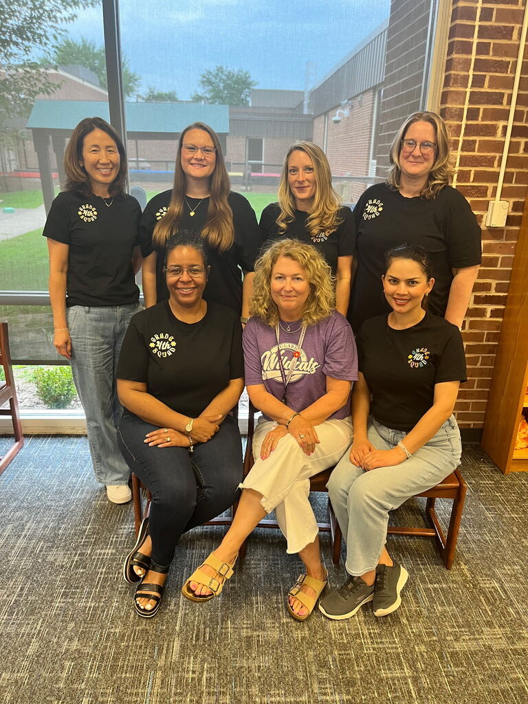 A group of eight women dressed in black T-shirts pose for a photo in front of a brick wall.