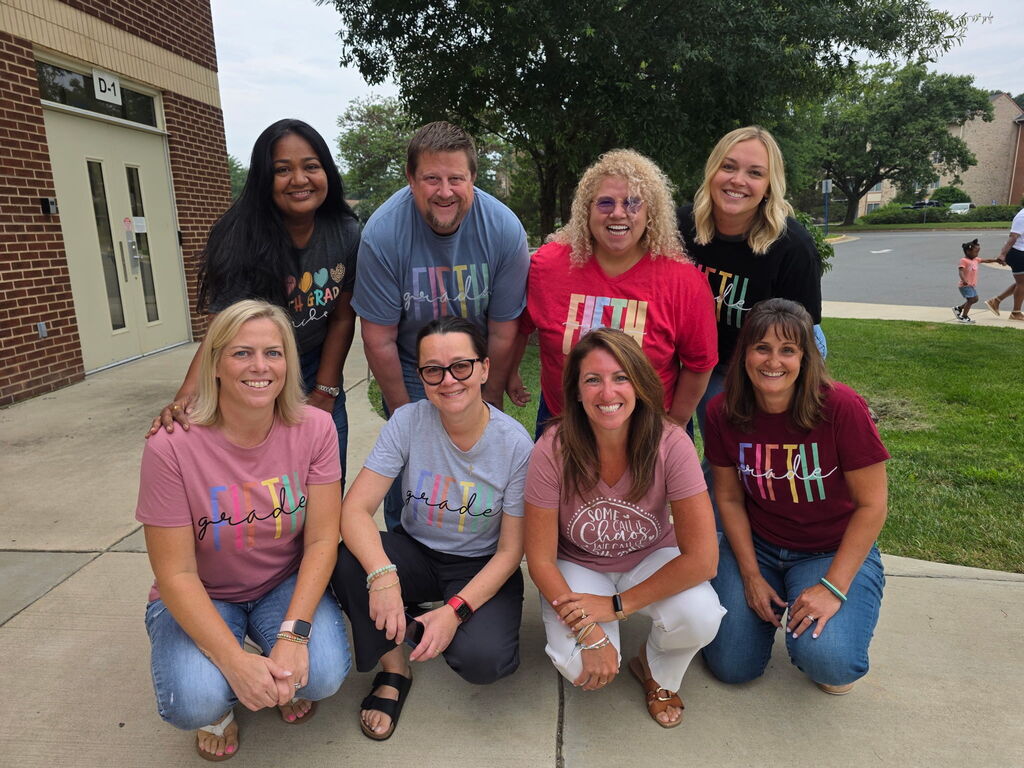 Eight people wearing matching pink t-shirts with "fifth" written on them are posing for a picture.