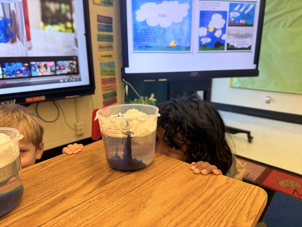 Two students looking at measuring cups  with water, food coloring, and shaving cream