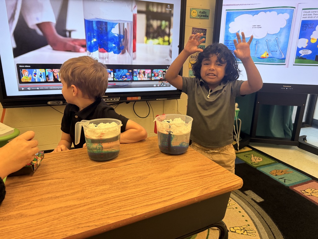 Two students in front of  measuring cups  with water, food coloring, and shaving cream