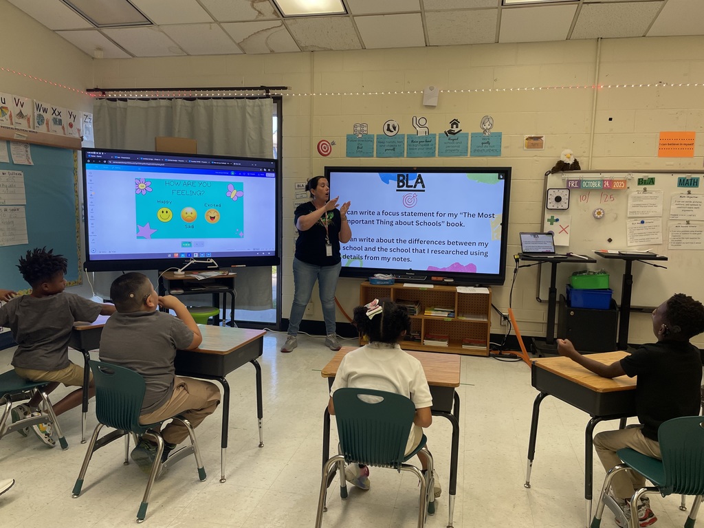 Teacher standing at the board, students sitting at desks looking at the board