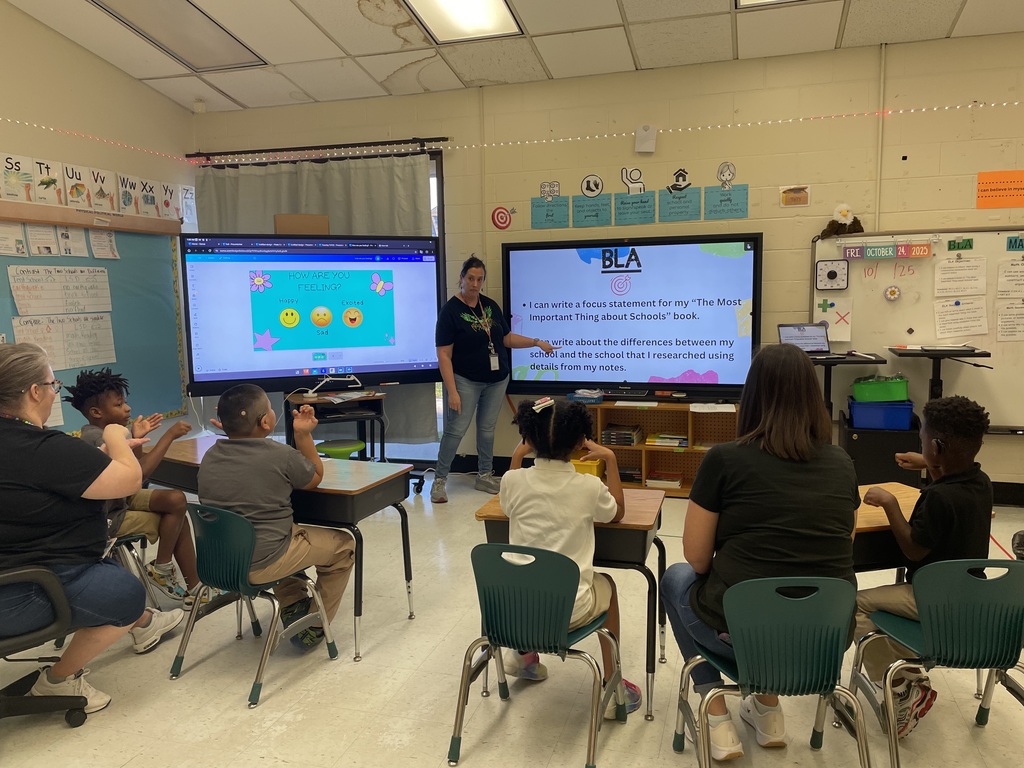 Teacher standing at the board, students sitting at desks looking at the board
