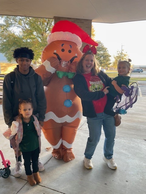 Three students and one staff posing next to an inflatable gingerbread man.