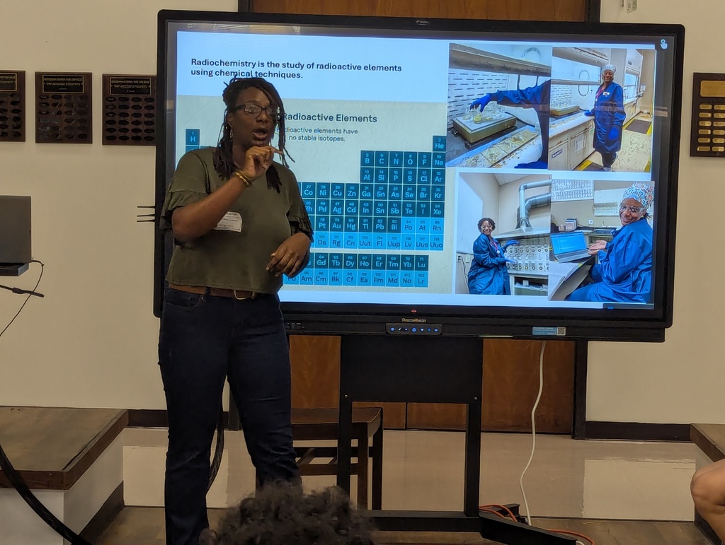 Career day presenter with periodic table of elements behind her