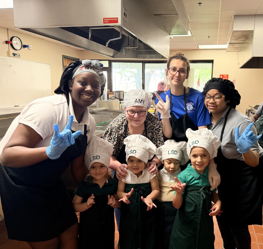 Students posing for a picture with aprons and chefs hats. 