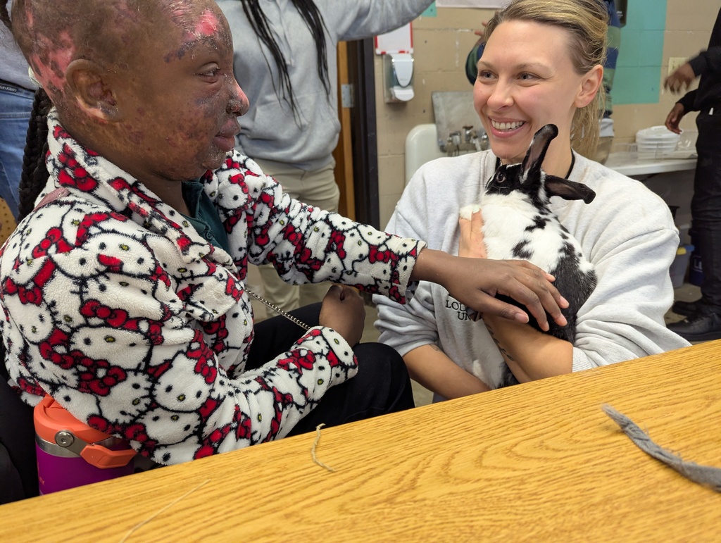 A staff member holding a bunny and a student petting it.