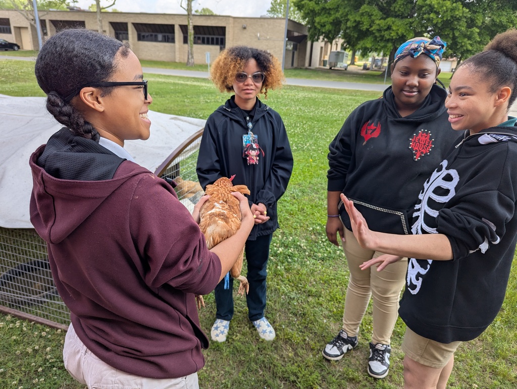 Students standing in a circle smiling with one student holding a chicken