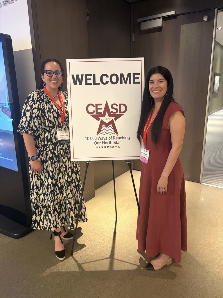 Two standing and smiling next to a CEASD sign.