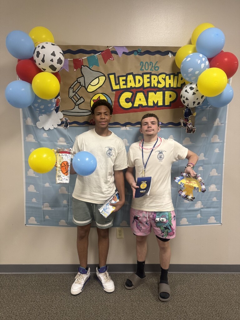 Students smiling and holding items in front of a leadership camp sign