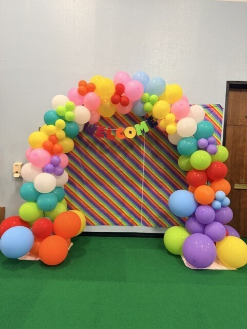 A colorful balloon arch in front of a welcome sign