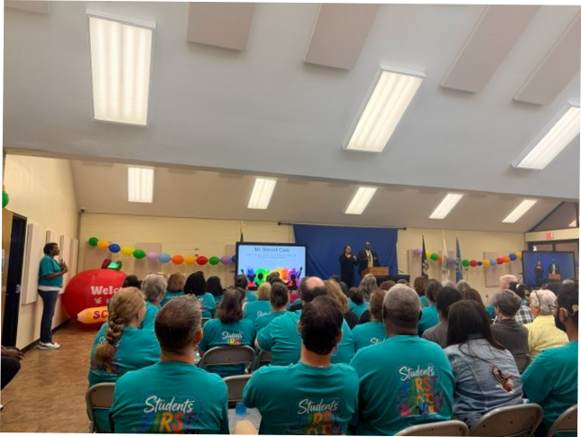 A view of the presnetation room for the Back to School event with staff wearing matching student first tshirts. Bernel Cook is presenting at the front of the room.