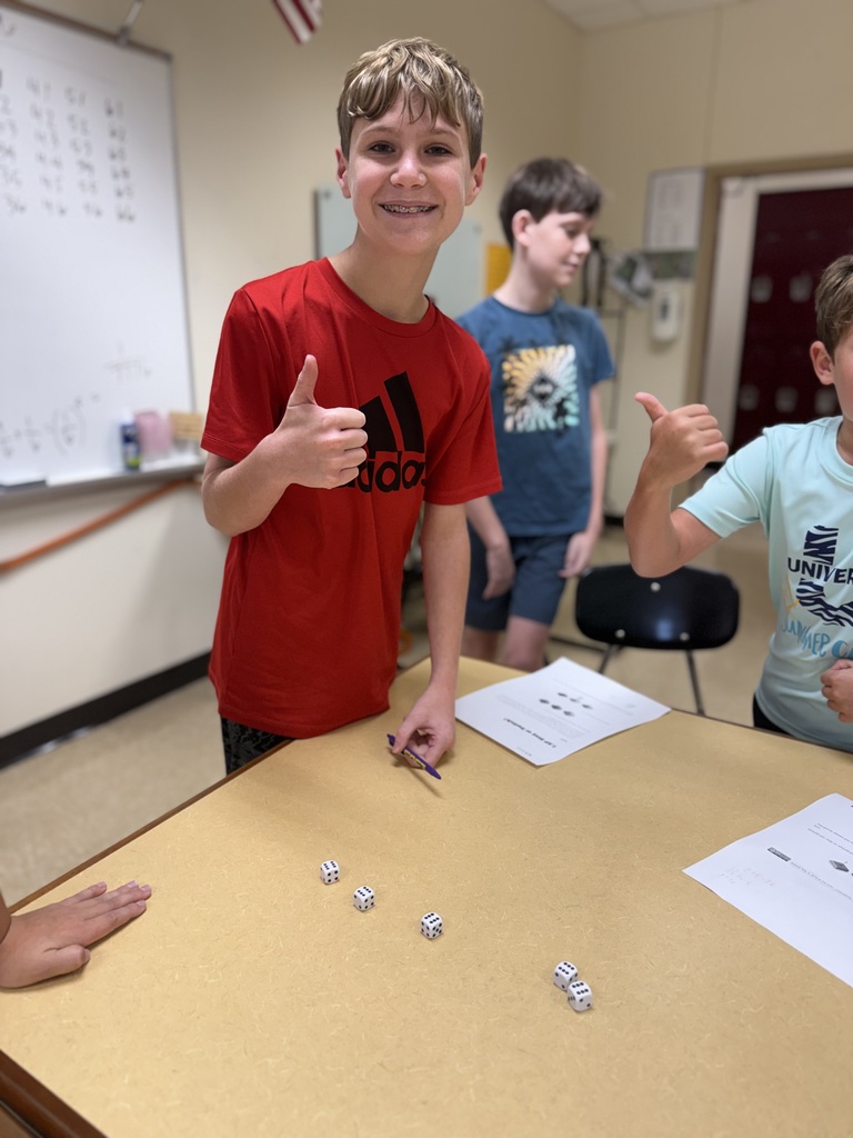 male student smiling with a thumbs up working on math at a classroom table