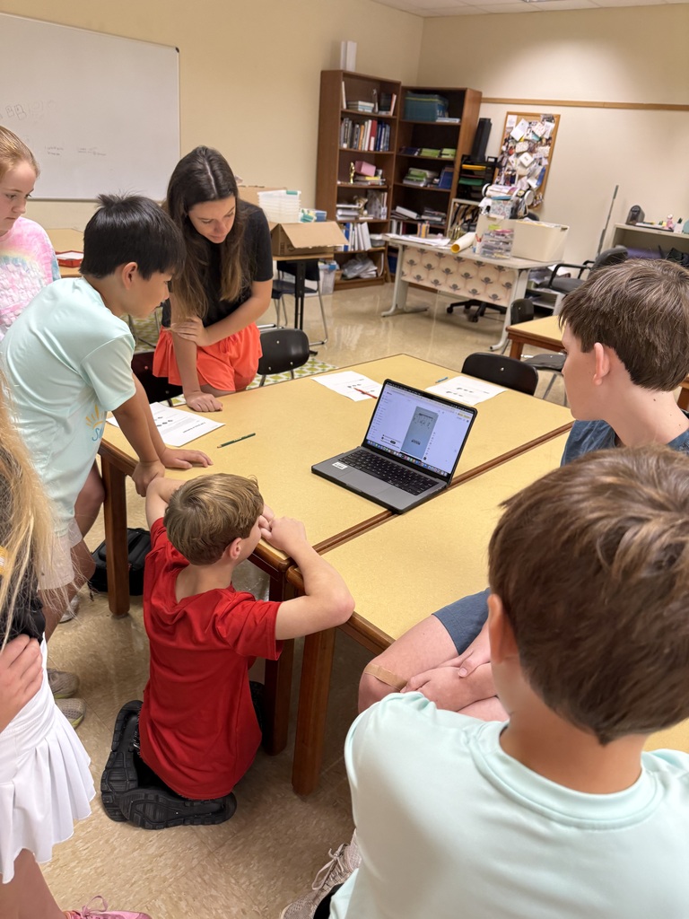 group of students seated around a table with female teacher learning from a laptop computer