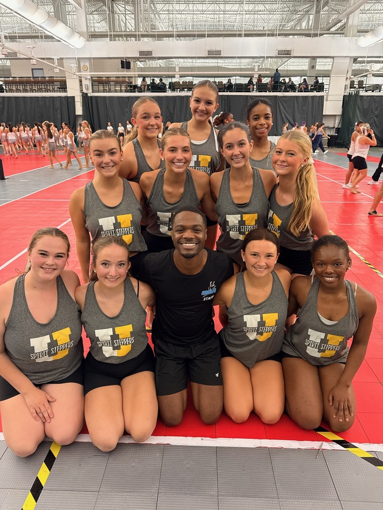 Girl dancers posed with male coach wearing grey tanks with "U" Spirit Steppers displayed