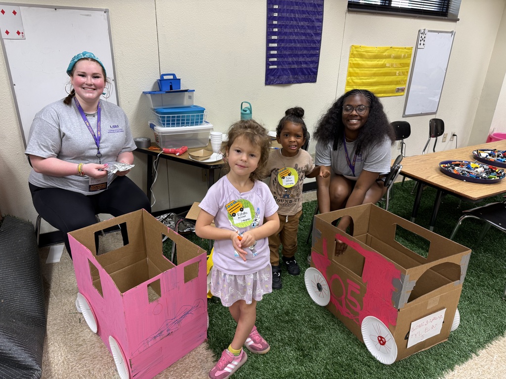 two college girls smiling at the camera with two little campers with cardboard car creations.