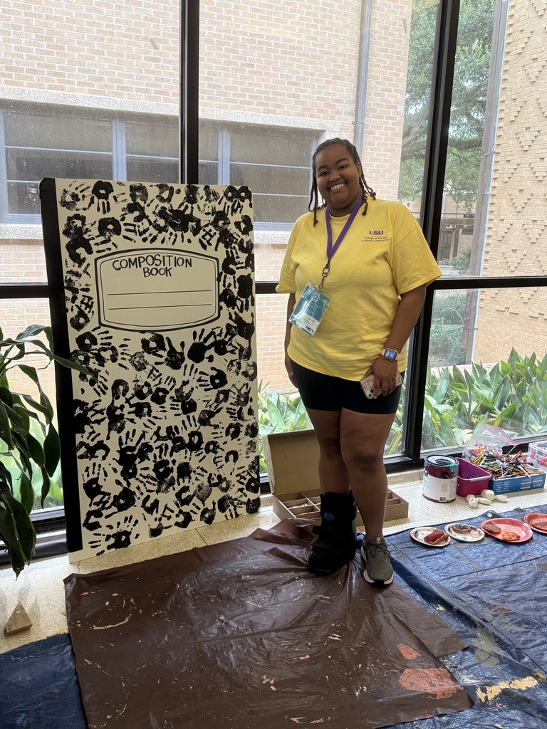 girl student standing beside a large composition notebook with black handprints all over.