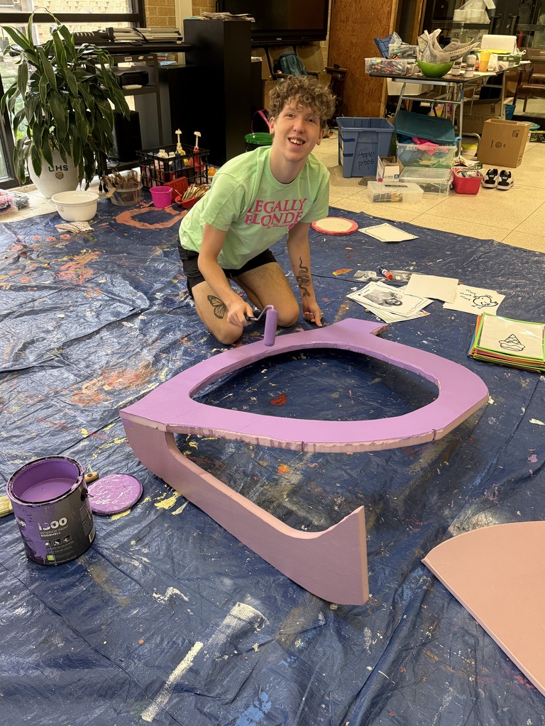 Camp student smiling at camera while paint a wooden object purple