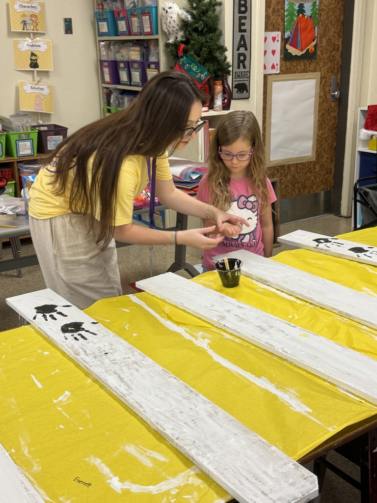 Two students leaning over a table covered in yellow doing handprints in brown paint