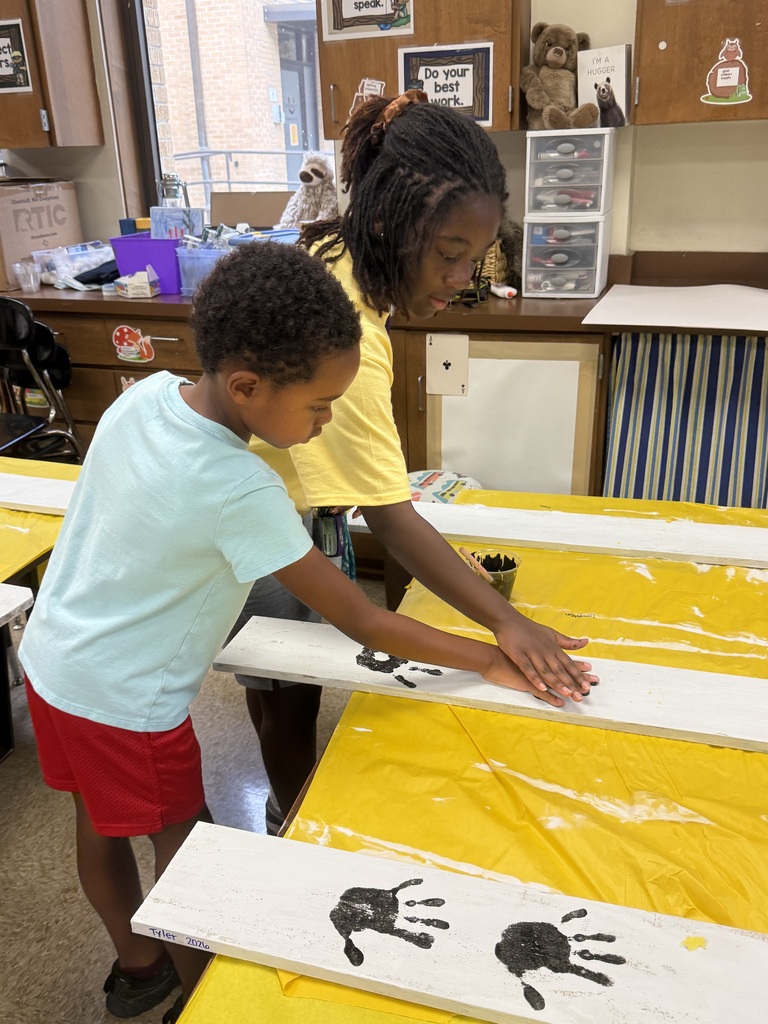 Two students leaning over a table covered in yellow doing handprints in brown paint