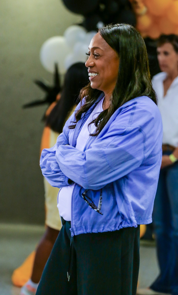 Smiling woman in a purple jacket stands indoors at a team event.