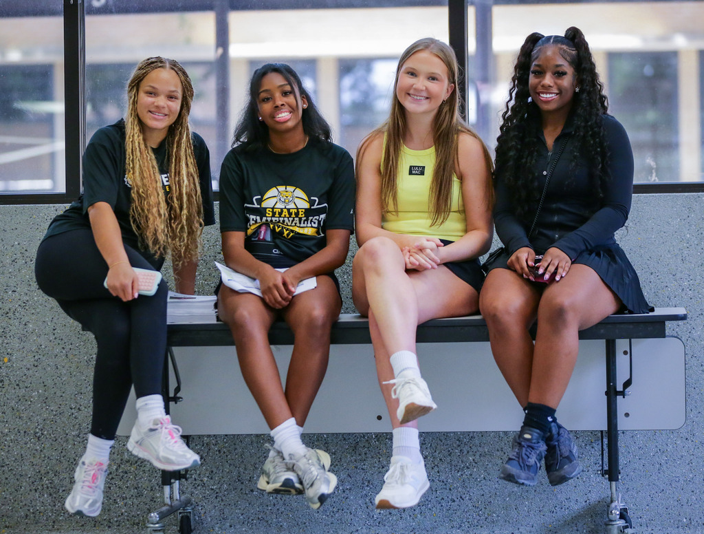 Four students sit together on a bench, smiling for a photo at a school event.
