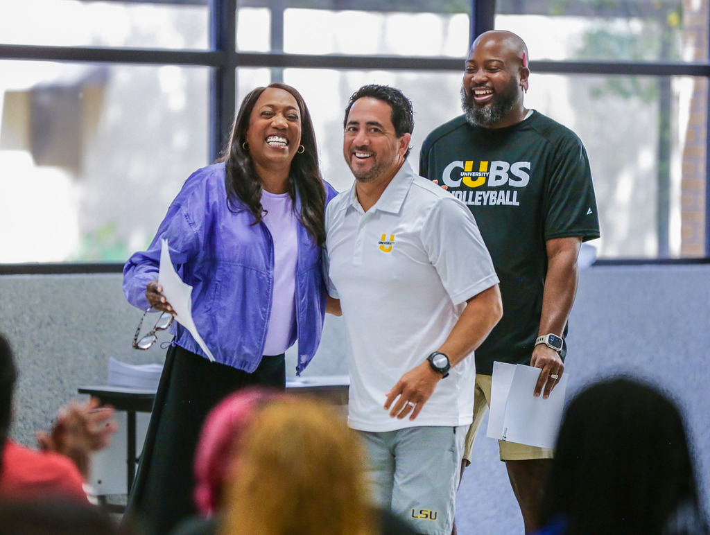 Three smiling people pose together indoors at a team event, with an audience blurred in the foreground.