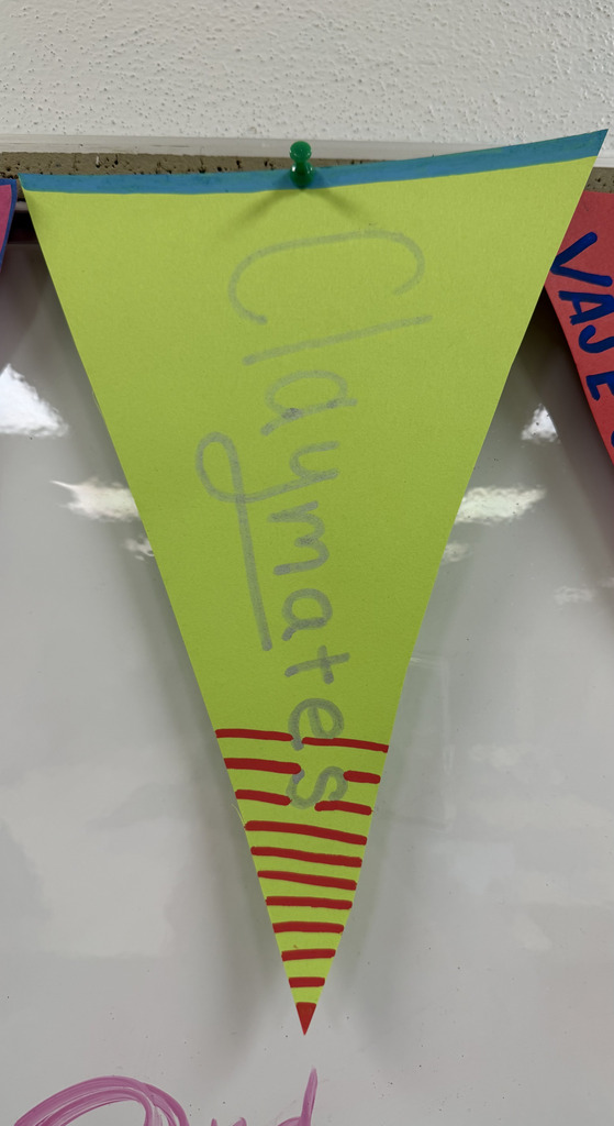 A lime green paper pennant hanging on a wall, decorated with red stripes at the bottom and silver text reading "Claymates."