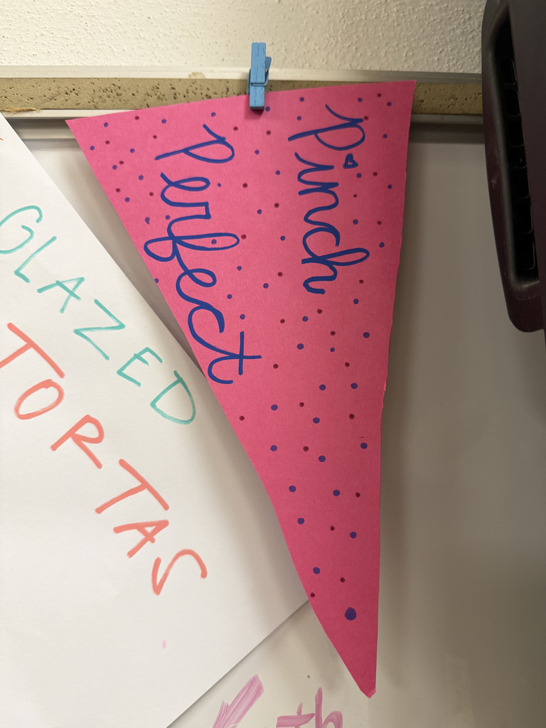 A pink paper pennant hanging vertically with purple dots and handwritten cursive text reading "Pinch Perfect."