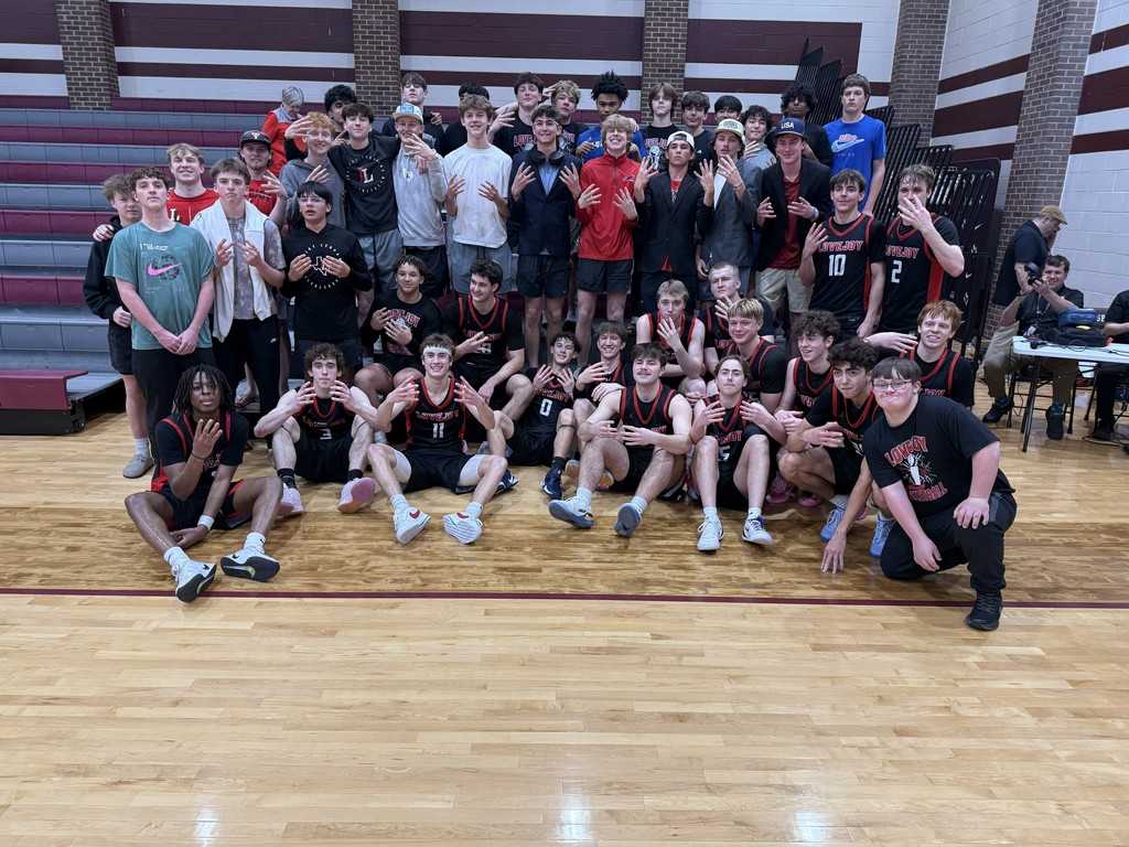A basketball team poses for a group photo on a court, with some players kneeling or crouching.