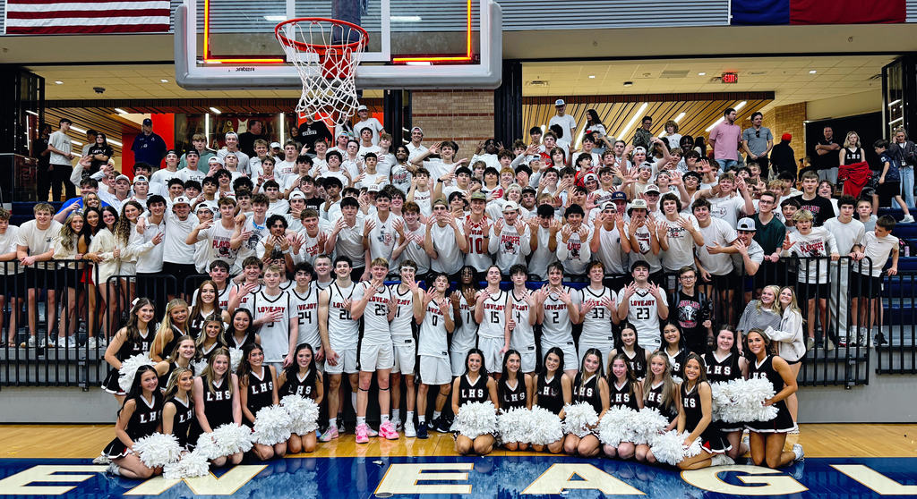 Basketball team poses with cheerleaders on a court with "Eagle" written on the floor.