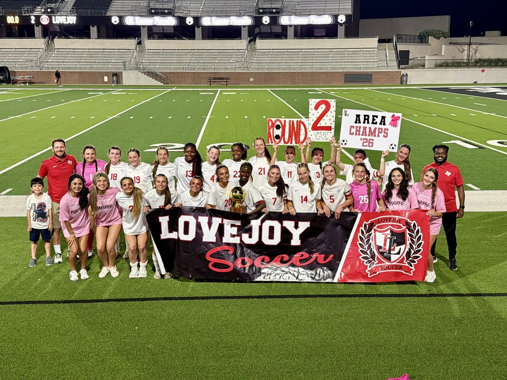 A group of soccer players and coaches stand on a field, holding signs and a banner.