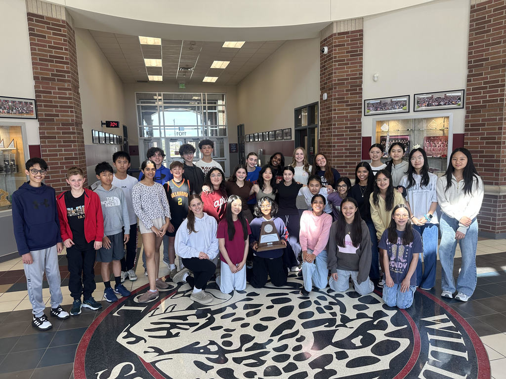 Group of students standing in a school hallway around a circular design on the floor.