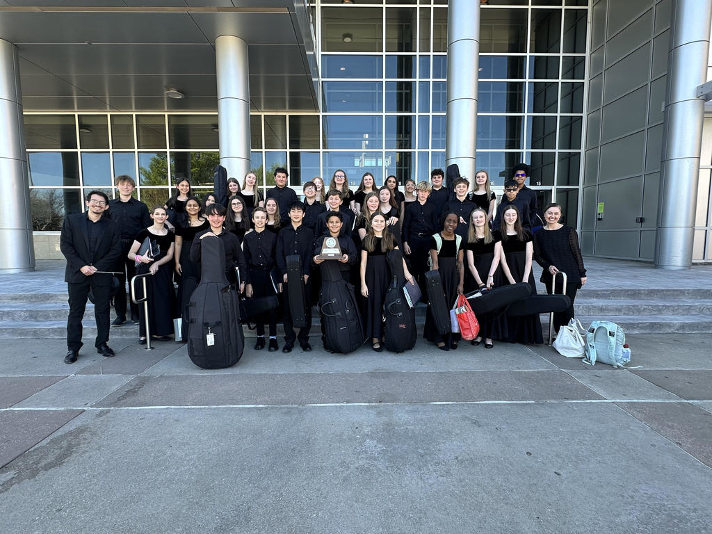 Group of people in black clothes and holding instruments, standing in front of a modern building.