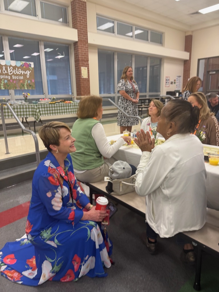 Adults are seated around tables in a room with a brick wall. Some are talking, and one is clapping.