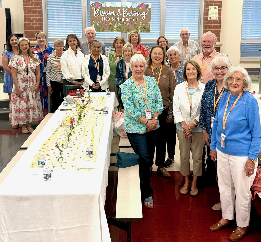 Group of people standing behind a long table with a white tablecloth, some wearing ID lanyards.