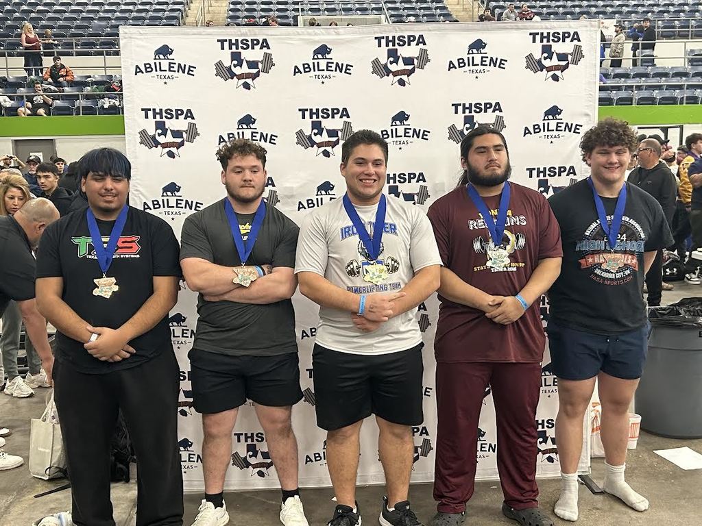 Five men stand together in front of a banner. They wear medals. One wears a white t-shirt, another a maroon shirt, and the others black shirts.