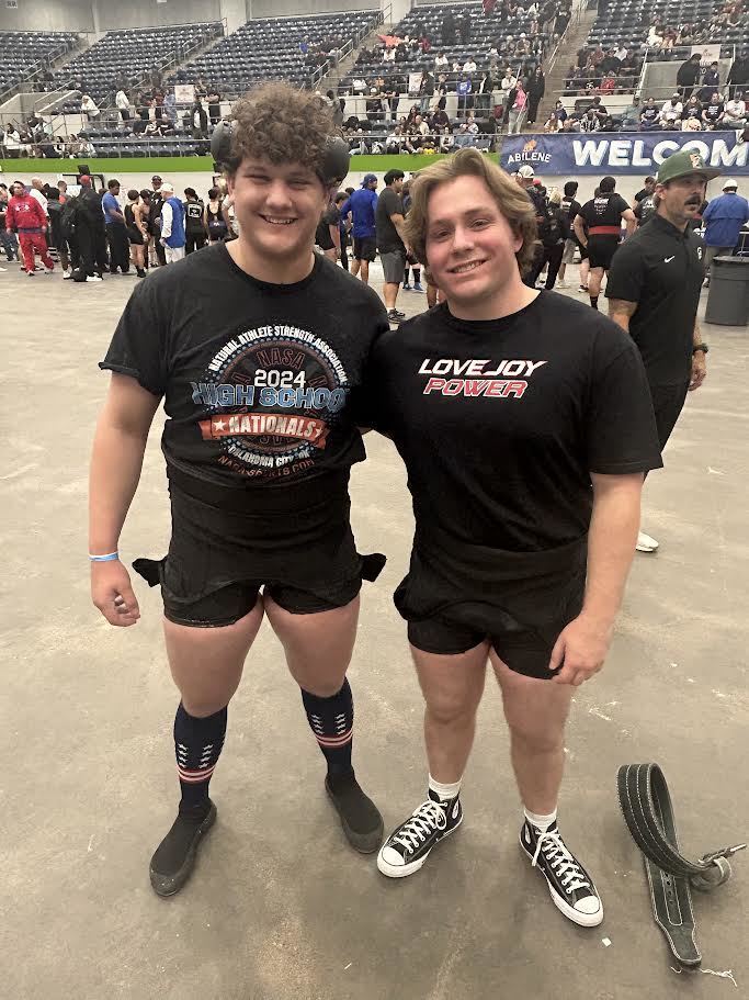 Two people in black shirts, shorts, and sneakers standing in an arena. One shirt reads "Love Joy Power."