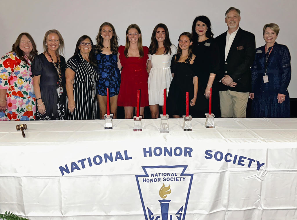 A group of people standing behind a table that reads "National Honor Society" with candles and a logo.