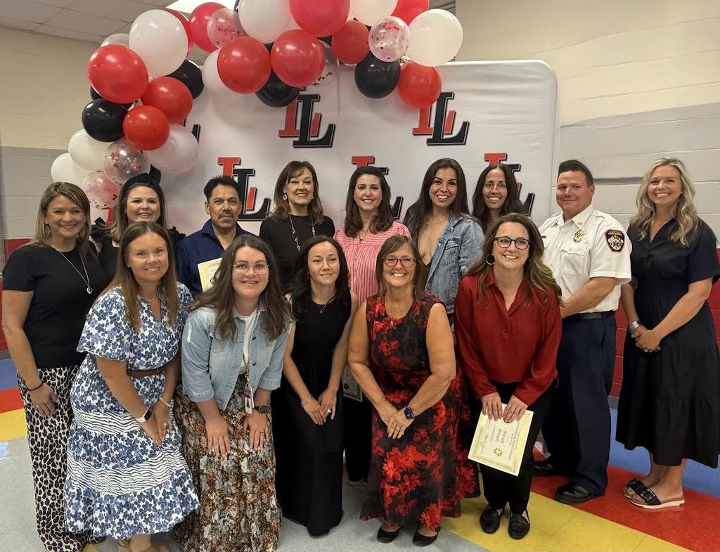 A group of people stand together with certificates in a room with balloons and a white backdrop.