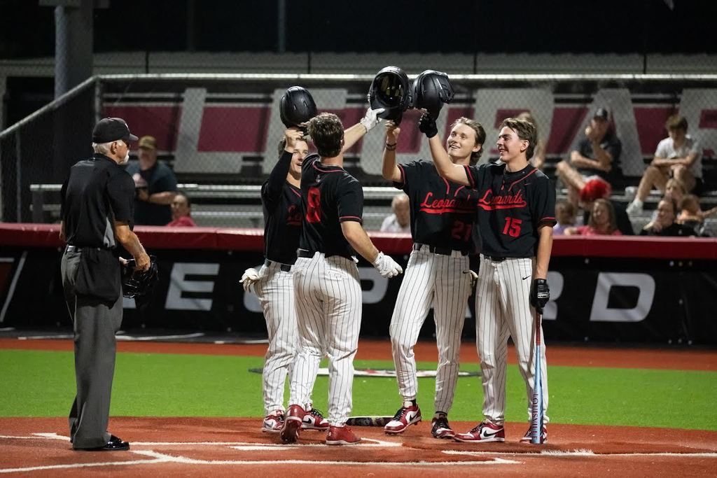 A team of players in black and white uniforms celebrate a win on a baseball field.