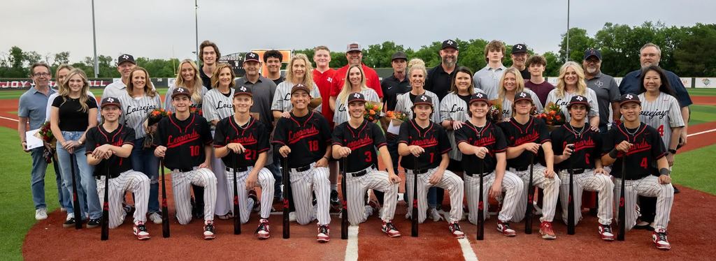 A group of individuals in baseball uniforms pose for a team photo on a baseball field.