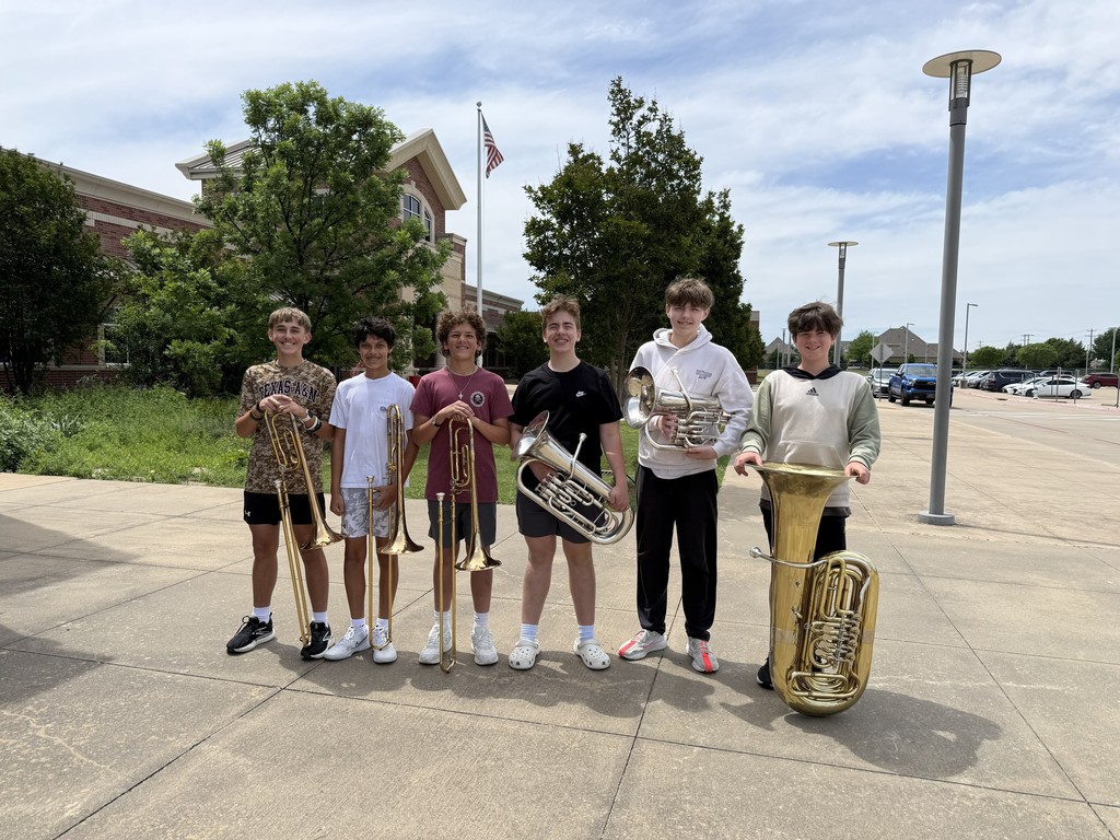 Six boys, each holding a different brass instrument, pose for a photo in a parking lot.