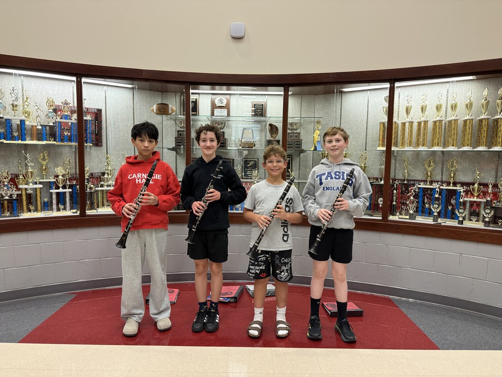 Four boys in a music room, each holding a clarinet, stand in front of a display case.