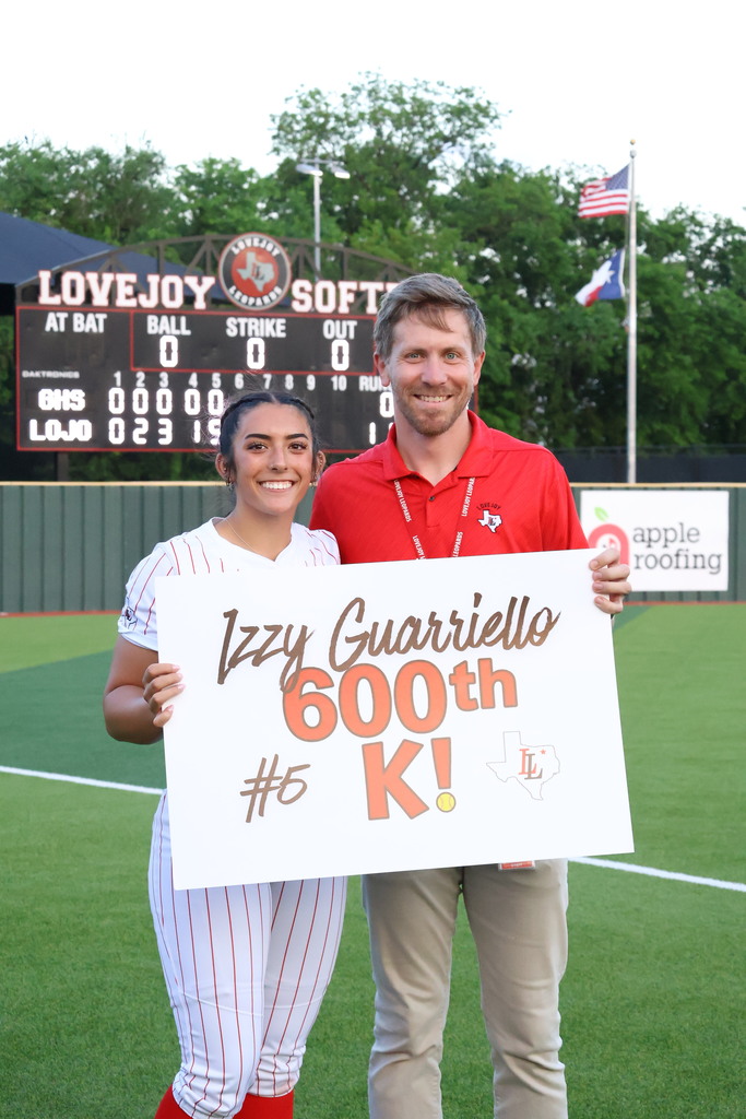 A woman and a man stand on a baseball field holding a sign that says "Izzy Guarriello 600th K!".