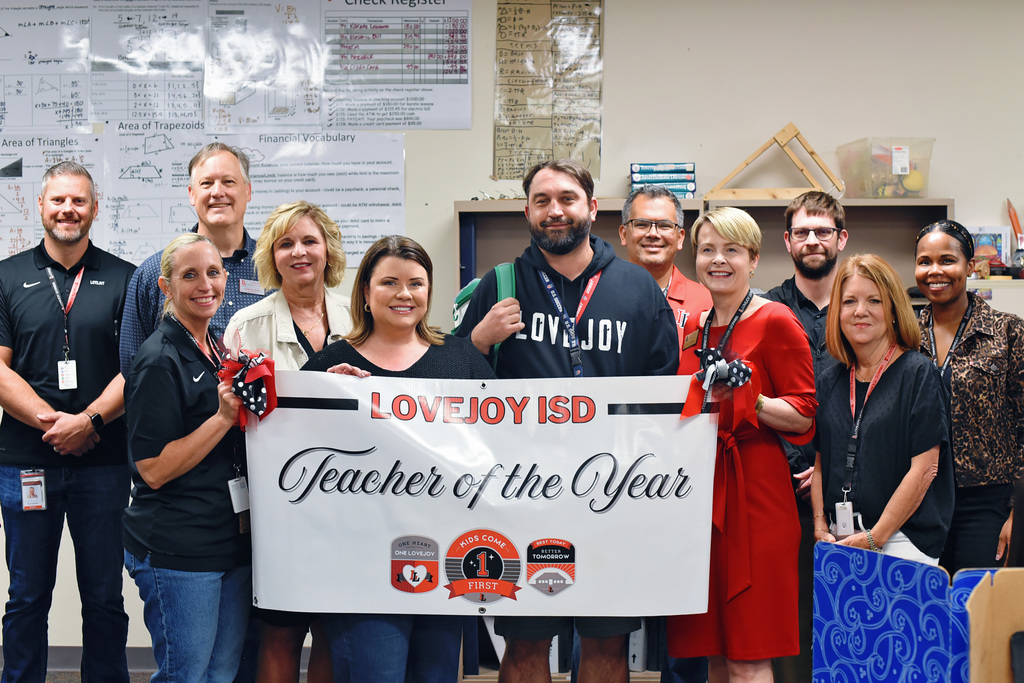 A group of people holding a banner with the words "Teacher of the Year" and other text.